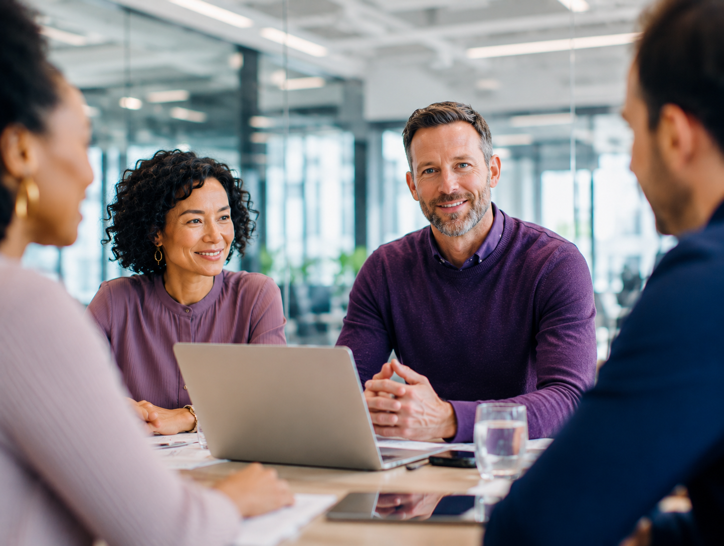 Vier professionals in gesprek rond een tafel in een moderne vergaderruimte, met een laptop centraal op tafel.