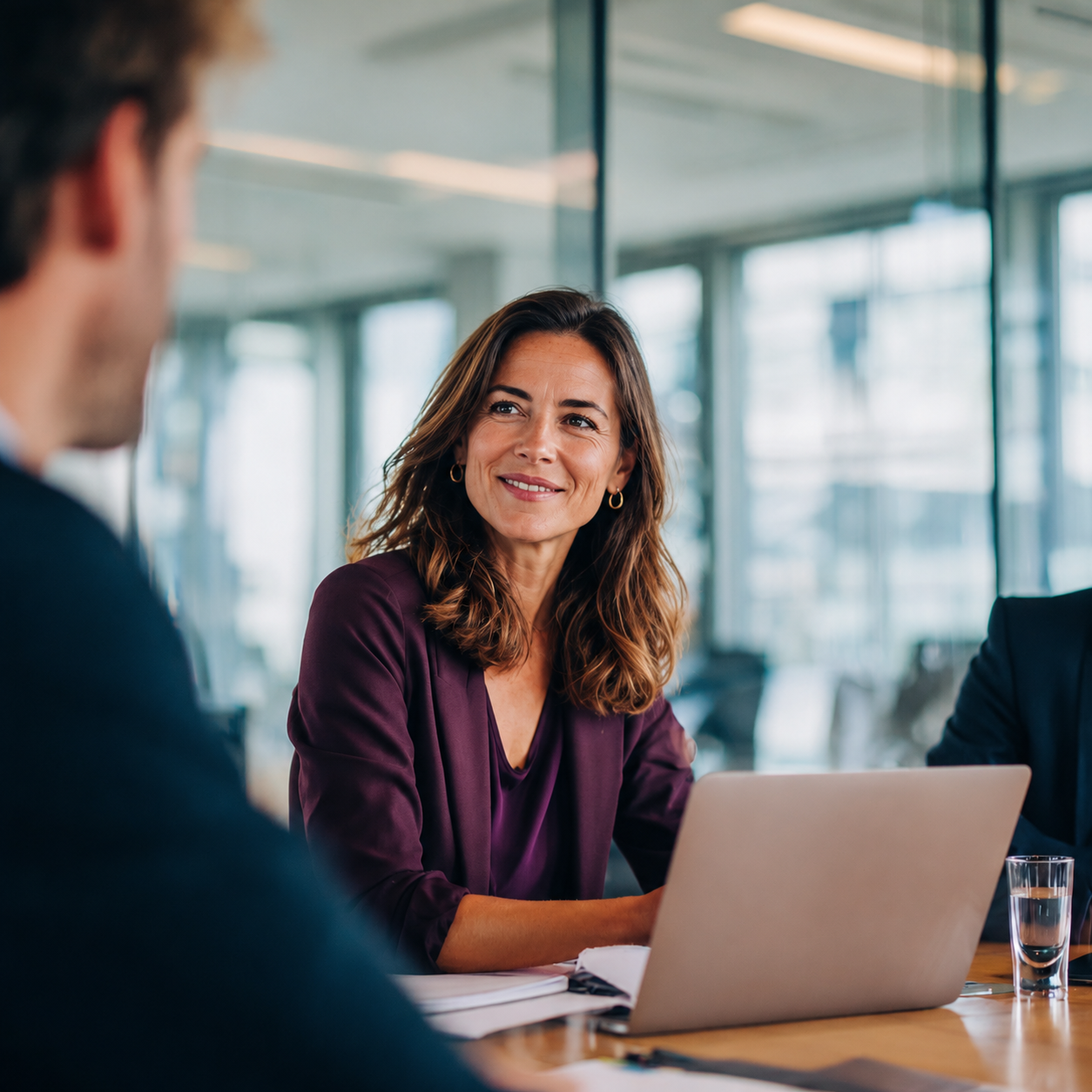 Vrouw in een paarse blazer voert een gesprek tijdens een vergadering met een laptop op tafel.