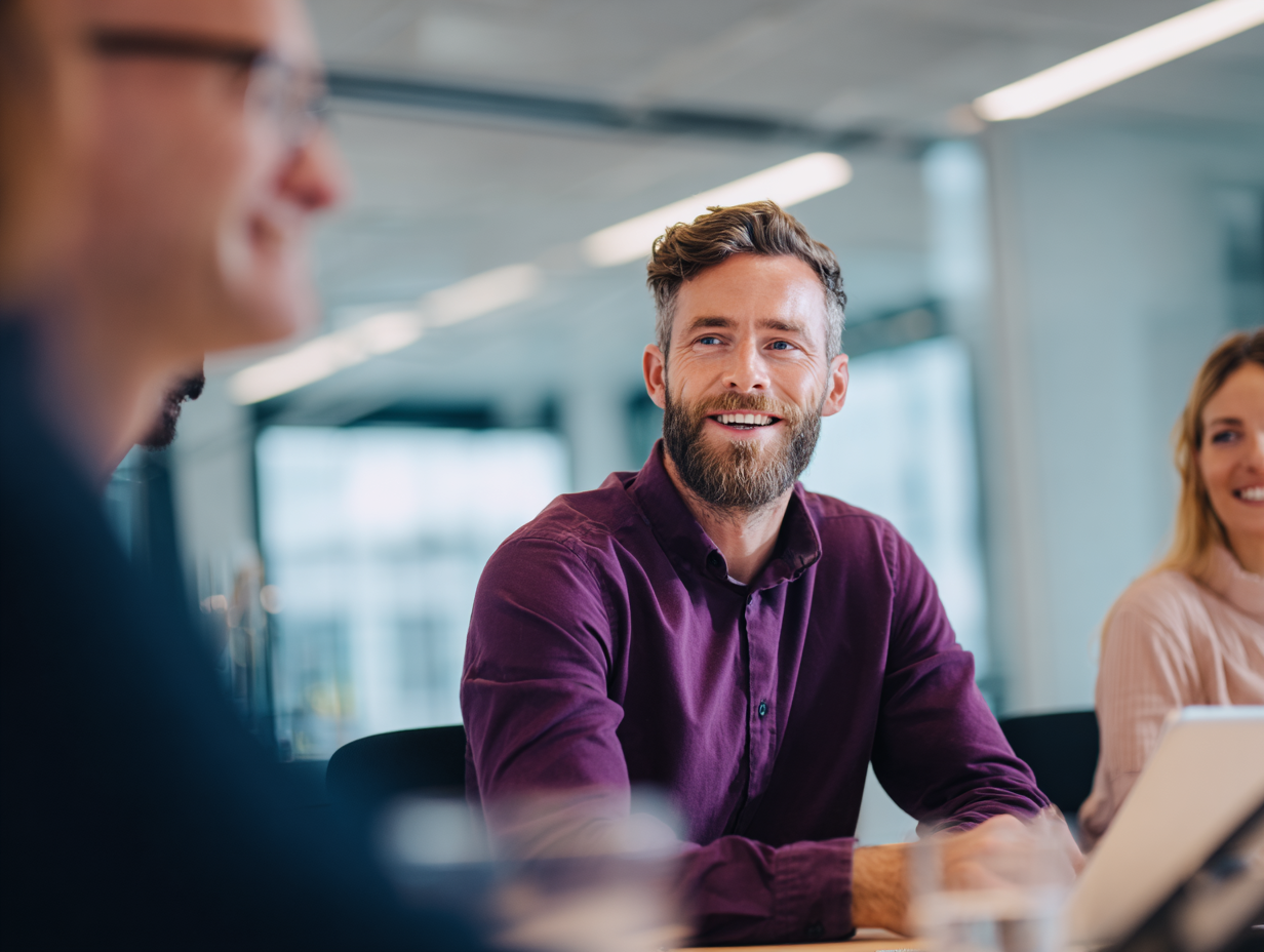Collega in een paars overhemd neemt actief deel aan een overleg met collega's.